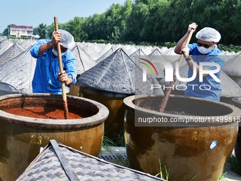 Workers use a wooden rake to turn sauces at the old soy sauce natural drying sauce shop in Yanhe Village, Rucheng Street, Rugao city, East C...