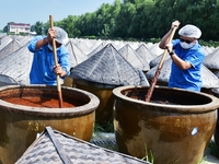 Workers use a wooden rake to turn sauces at the old soy sauce natural drying sauce shop in Yanhe Village, Rucheng Street, Rugao city, East C...