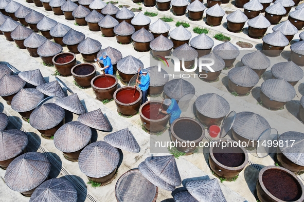 Workers use a wooden rake to turn sauces at the old soy sauce natural drying sauce shop in Yanhe Village, Rucheng Street, Rugao city, East C...