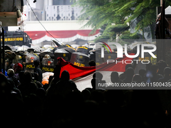 Thousands of demonstrators clash with police while holding Indonesian flags during a protest against the revision of the Regional Head Elect...