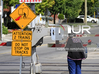 A pedestrian waits for a passenger commuter train to pass on a level crossing on the same rail corridor through the Brampton Innovation Dist...