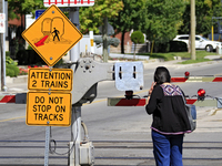 A pedestrian waits for a passenger commuter train to pass on a level crossing on the same rail corridor through the Brampton Innovation Dist...