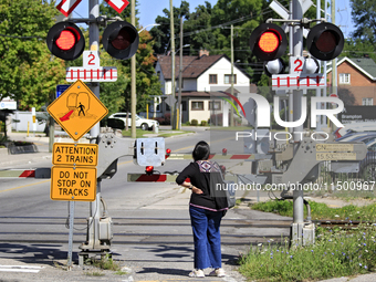 A pedestrian waits for a passenger commuter train to pass on a level crossing on the same rail corridor through the Brampton Innovation Dist...