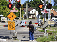 A pedestrian waits for a passenger commuter train to pass on a level crossing on the same rail corridor through the Brampton Innovation Dist...