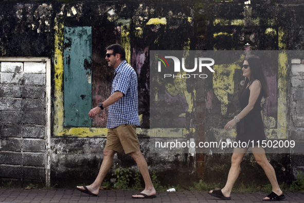 Foreign tourists walk past wall art depicting a fading Sri Lanka flag near Colombo, Sri Lanka, on August 23, 2024. According to a world repo...