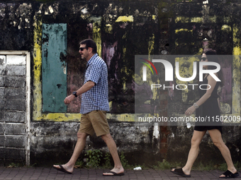 Foreign tourists walk past wall art depicting a fading Sri Lanka flag near Colombo, Sri Lanka, on August 23, 2024. According to a world repo...