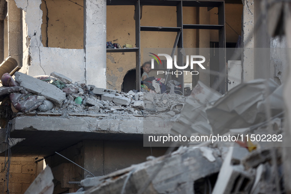 A Palestinian girl stands in despair on the balcony of a damaged apartment near a building destroyed by an Israeli airstrike in the Nuseirat...