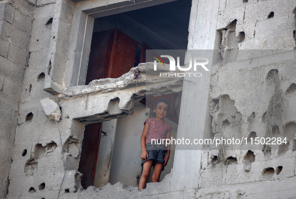 A Palestinian girl stands in despair on the balcony of a damaged apartment near a building destroyed by an Israeli airstrike in the Nuseirat...