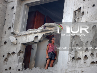 A Palestinian girl stands in despair on the balcony of a damaged apartment near a building destroyed by an Israeli airstrike in the Nuseirat...