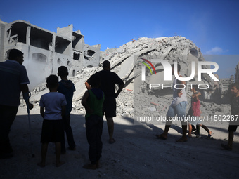 Palestinians gather near a building destroyed by an Israeli airstrike in the Nuseirat refugee camp in central Gaza Strip on August 23, 2024,...