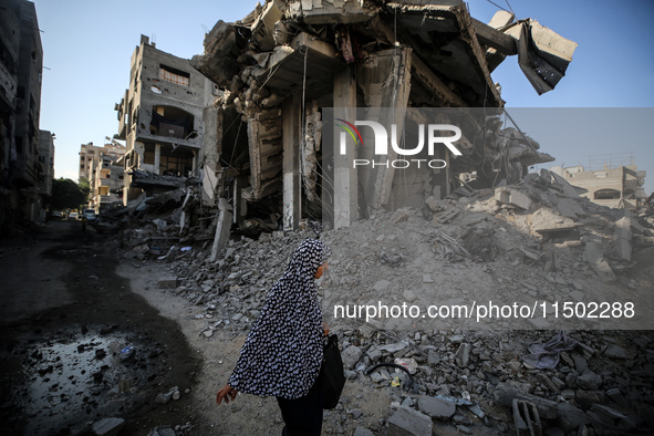 A Palestinian woman walks near a building destroyed by an Israeli airstrike in the Nuseirat refugee camp in central Gaza Strip on August 23,...