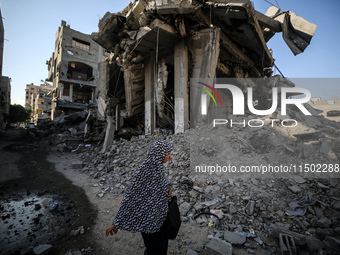 A Palestinian woman walks near a building destroyed by an Israeli airstrike in the Nuseirat refugee camp in central Gaza Strip on August 23,...