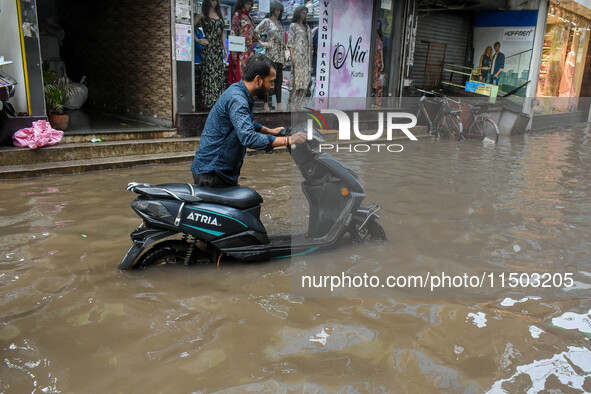 A man navigates his electric scooter through a flooded road caused by heavy rain in Kolkata, India, on August 23, 2024. 