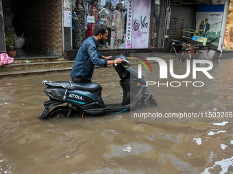 A man navigates his electric scooter through a flooded road caused by heavy rain in Kolkata, India, on August 23, 2024. (