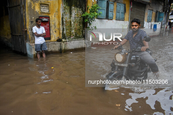 A man rides his bike through a flooded road caused by heavy rain in Kolkata, India, on August 23, 2024. 