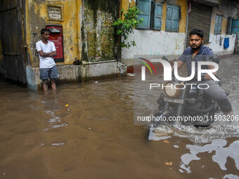 A man rides his bike through a flooded road caused by heavy rain in Kolkata, India, on August 23, 2024. (