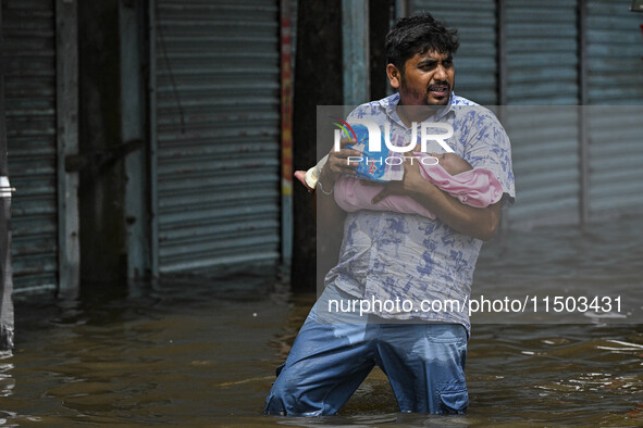 A man with his child wades through floodwaters in the Mohipal area of Feni district in Chittagong division, Bangladesh, on August 23, 2024....