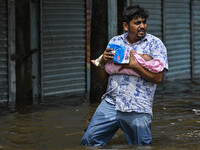 A man with his child wades through floodwaters in the Mohipal area of Feni district in Chittagong division, Bangladesh, on August 23, 2024....