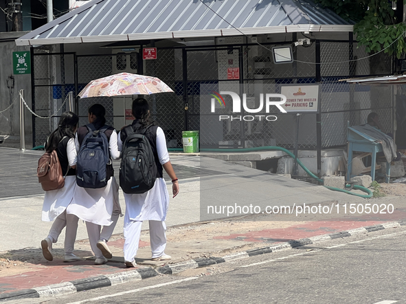 Schoolgirls share an umbrella to protect themselves from the hot sun while walking along the footpath in Thiruvananthapuram (Trivandrum), Ke...