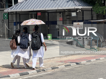 Schoolgirls share an umbrella to protect themselves from the hot sun while walking along the footpath in Thiruvananthapuram (Trivandrum), Ke...