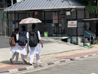 Schoolgirls share an umbrella to protect themselves from the hot sun while walking along the footpath in Thiruvananthapuram (Trivandrum), Ke...