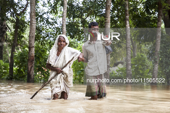 Pedestrians wade through flooded roads in floodwaters up to their waists and knees in Bishumia Hat, Mirsarai, southern Bangladesh. At least...