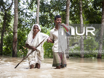 Pedestrians wade through flooded roads in floodwaters up to their waists and knees in Bishumia Hat, Mirsarai, southern Bangladesh. At least...