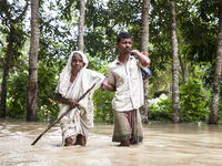 Pedestrians wade through flooded roads in floodwaters up to their waists and knees in Bishumia Hat, Mirsarai, southern Bangladesh. At least...