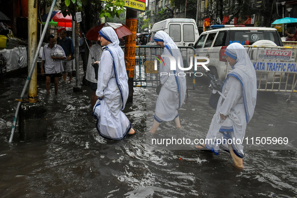 Sisters of the Missionaries of Charity make their way through a flooded street amidst heavy torrential downpour in Kolkata, India, on August...