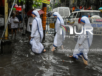 Sisters of the Missionaries of Charity make their way through a flooded street amidst heavy torrential downpour in Kolkata, India, on August...