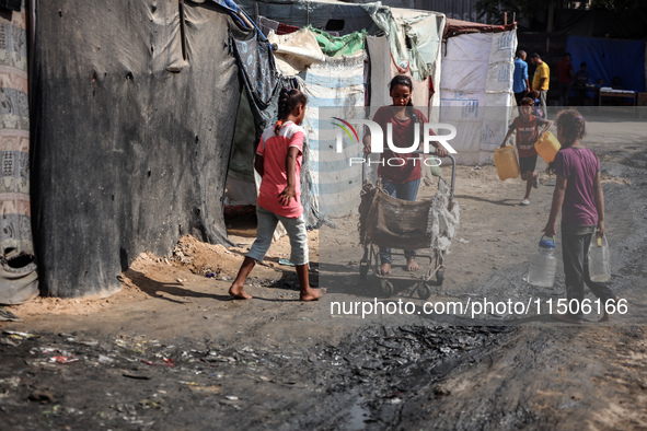 Displaced Palestinian children carry containers to fill with water at a makeshift displacement camp in Deir el-Balah in the central Gaza Str...