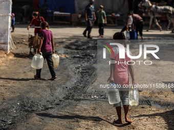 Displaced Palestinian children carry containers to fill with water at a makeshift displacement camp in Deir el-Balah in the central Gaza Str...