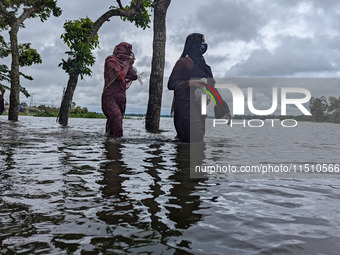 People wade through floodwaters in Feni, Bangladesh, on August 25, 2024. (