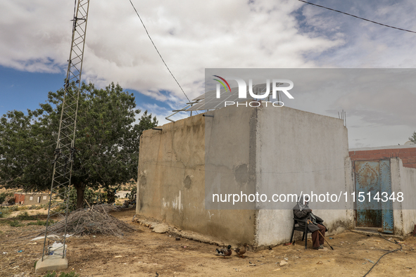 An older farmer sits by a water well whose motor is powered by photovoltaic energy to irrigate his field in a rural area in Kairouan, Tunisi...