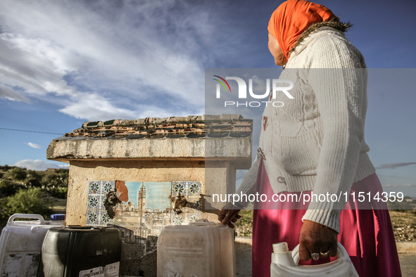 A rural woman fills plastic cans with water at a drinking water point in the isolated rural area of Chrichira located in Kairouan, Tunisia,...