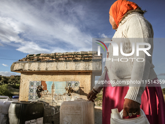 A rural woman fills plastic cans with water at a drinking water point in the isolated rural area of Chrichira located in Kairouan, Tunisia,...