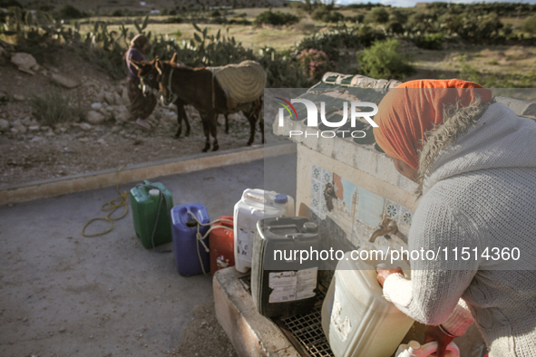 A rural woman fills plastic cans with water at a drinking water point in the isolated rural area of Chrichira located in Kairouan, Tunisia,...