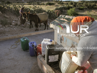 A rural woman fills plastic cans with water at a drinking water point in the isolated rural area of Chrichira located in Kairouan, Tunisia,...