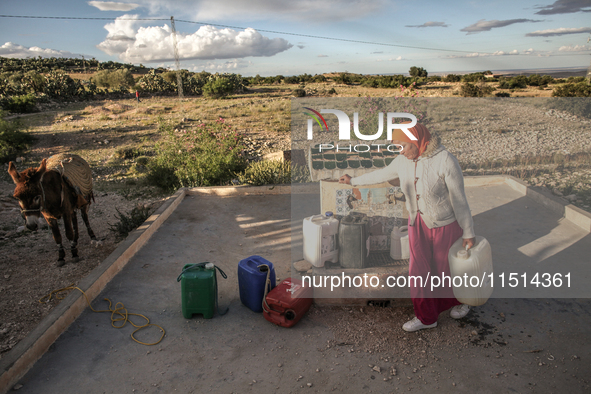 A rural woman carries plastic cans filled with water on the back of her donkey at a drinking water point in the isolated rural area of Chric...