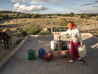 A rural woman carries plastic cans filled with water on the back of her donkey at a drinking water point in the isolated rural area of Chric...