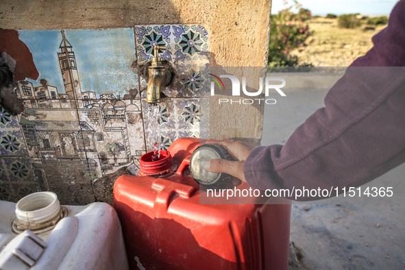 A rural woman fills plastic cans with water at a drinking water point in the isolated rural area of Chrichira located in Kairouan, Tunisia,...