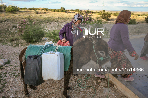 Rural women load jerry cans full of water on the back of a donkey at a drinking water point in the isolated rural area of Chrichira located...