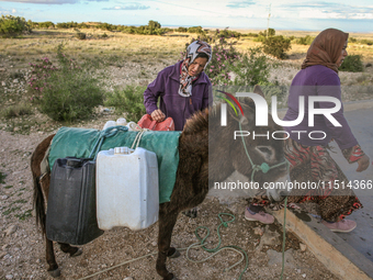 Rural women load jerry cans full of water on the back of a donkey at a drinking water point in the isolated rural area of Chrichira located...