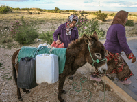 Rural women load jerry cans full of water on the back of a donkey at a drinking water point in the isolated rural area of Chrichira located...