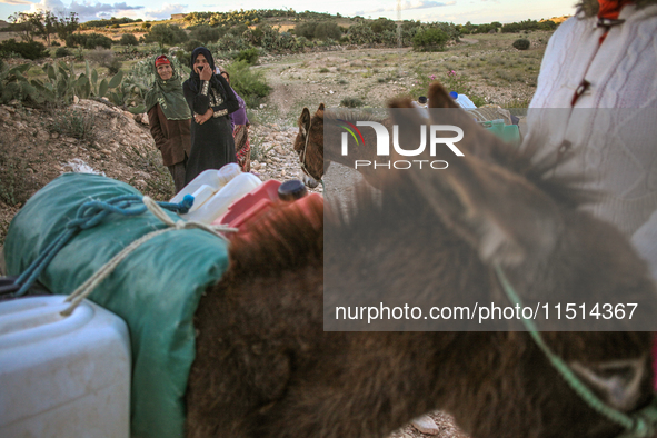 Rural women load jerry cans full of water on the back of a donkey at a drinking water point in the isolated rural area of Chrichira located...