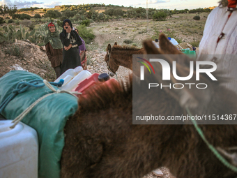 Rural women load jerry cans full of water on the back of a donkey at a drinking water point in the isolated rural area of Chrichira located...