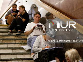 People sit on the steps of an interchange passage at the Teatralna metro station during the massive Russian drone and missile attack on Ukra...