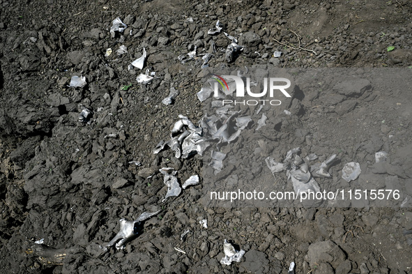 The fragments of a Russian projectile are arranged on the edge of the crater near the house of a man who is killed by the Russian missile at...