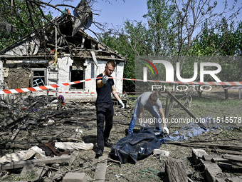 Two men take care of the body of a man in the human remains pouch outside the victim's house after the fatal Russian missile attack in the Z...