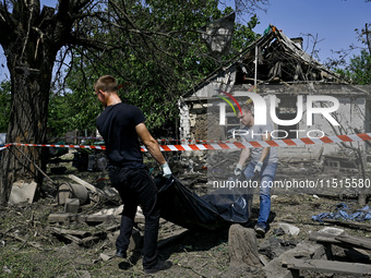 Two men take care of the body of a man in the human remains pouch outside the victim's house after the fatal Russian missile attack in the Z...